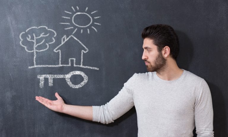 Man gesturing toward chalkboard drawing of a home and key to home