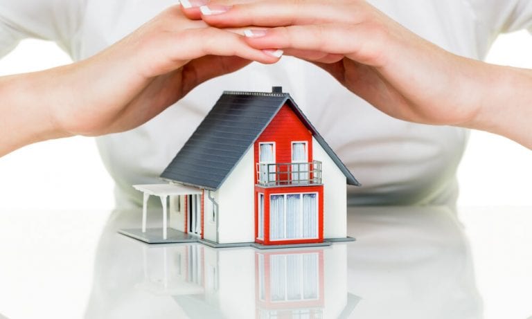 Woman protecting model home with her hands cupped above it