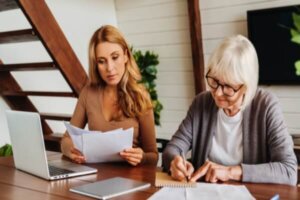 Senior woman with help of her daughter making bills at home, paying debt.