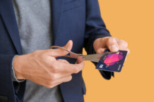 Businessman cutting credit card on color background, closeup representing a charge-off.